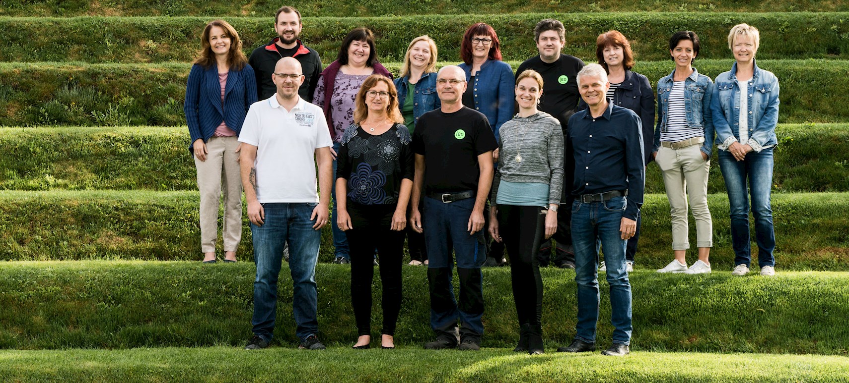 14 Personen vom Leo Team stehen in zwei Reihen auf terrassenförmig angeordneten Rasenstufen.