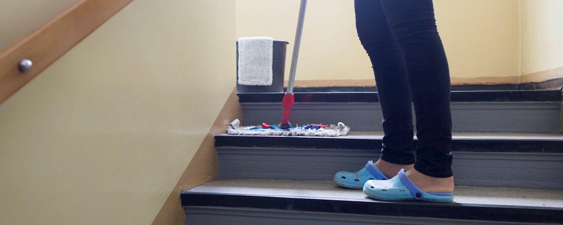 Frau in langer, schwarzer Hose, reinigt eine Stiege mit einem Wischmop.