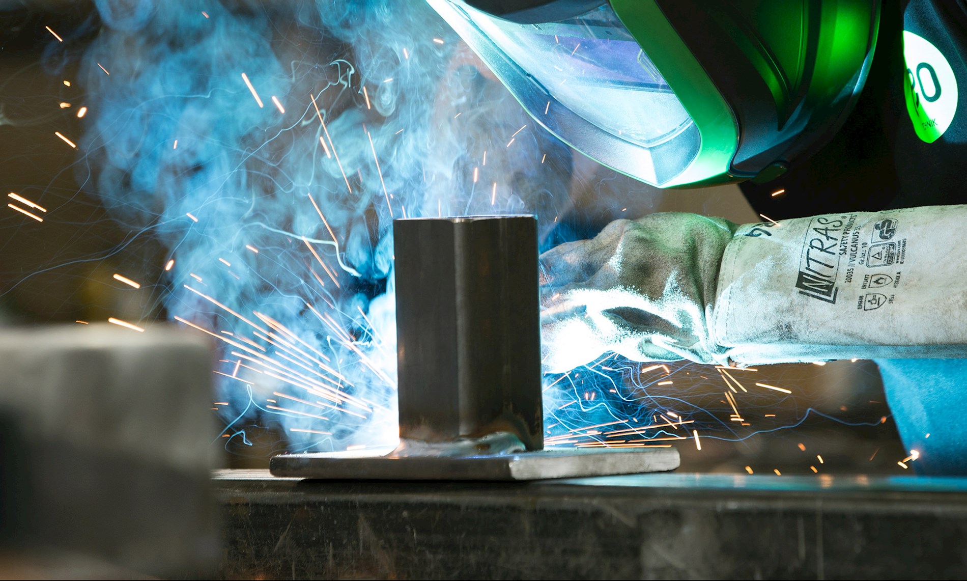 A person is welding in a workshop. He is wearing a face shield to protect the eyes and the face from the bright light.