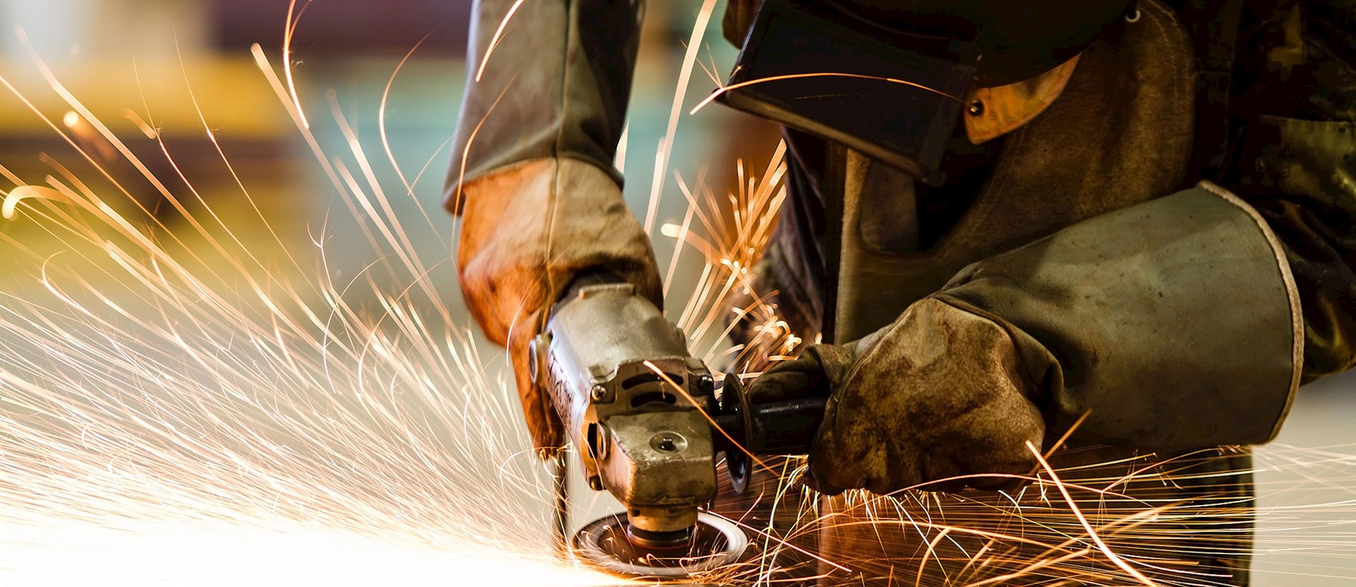 A person is grinding a piece of metal. You can see sparks. The person is wearing gloves to be safe.
