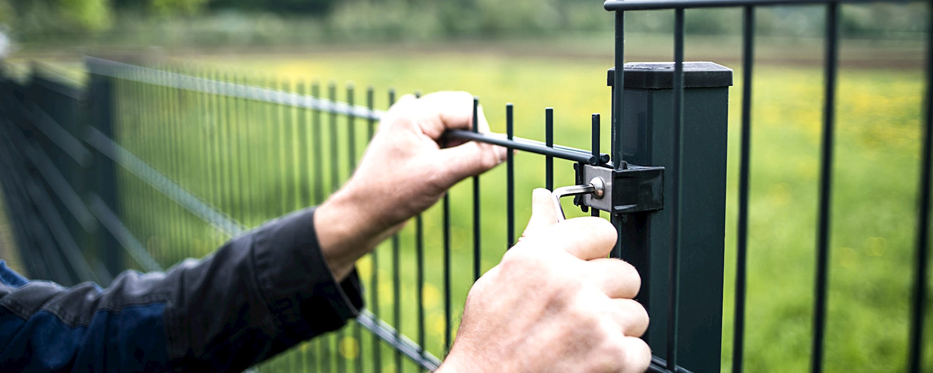 You can see the hands of a person. They are screwing a piece of fence to a fence post.