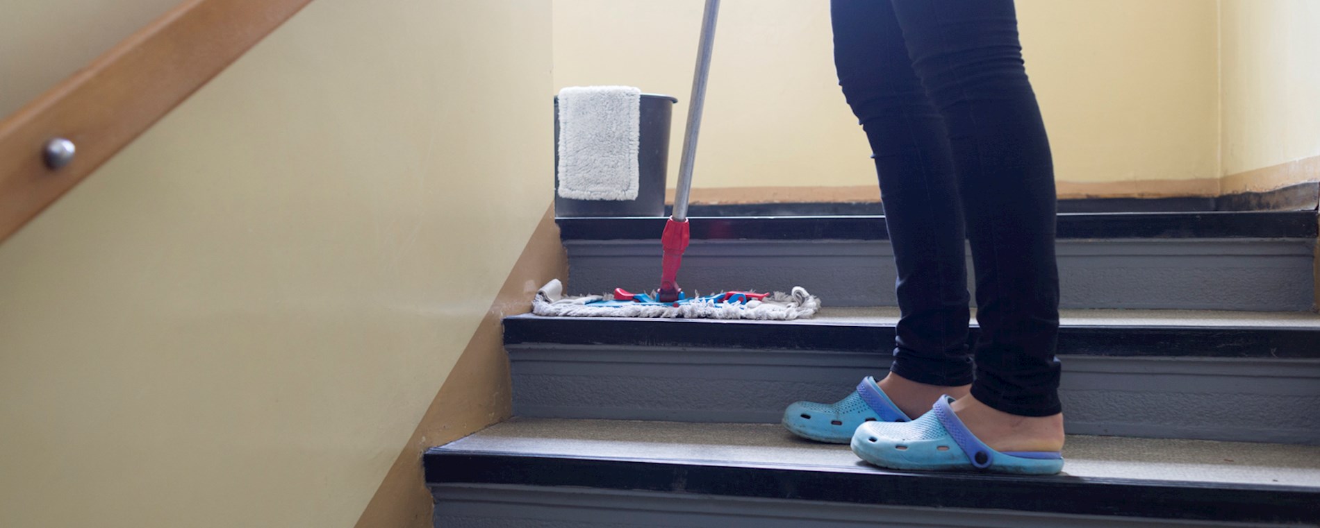 You can see a person’s legs. They are wearing black trousers. They are cleaning stairs with a mop.