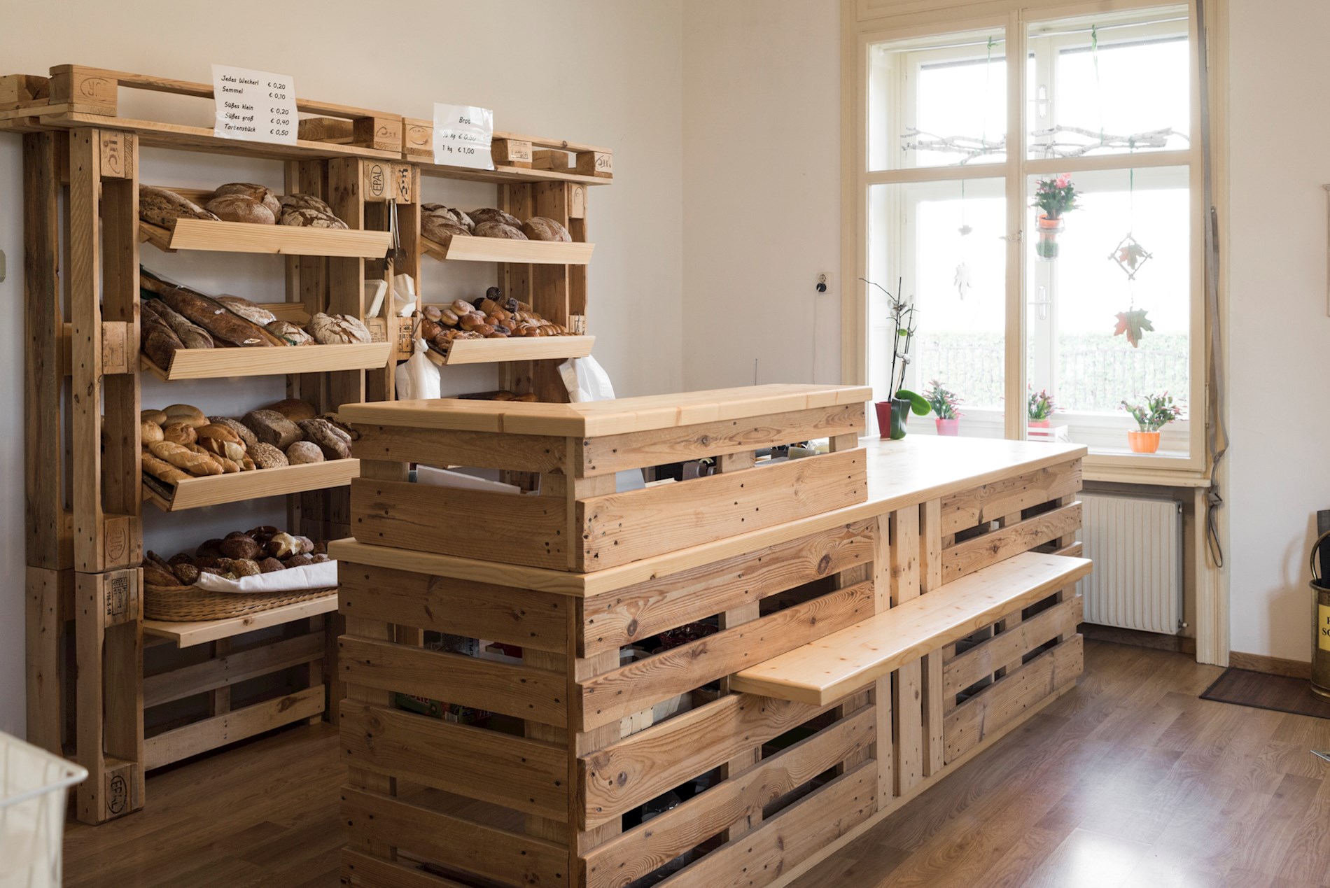 You can see beautiful, neat shelves made from wood. They are in the social supermarket in Fürstenfeld. On the shelves, there is fresh bread and pastry.