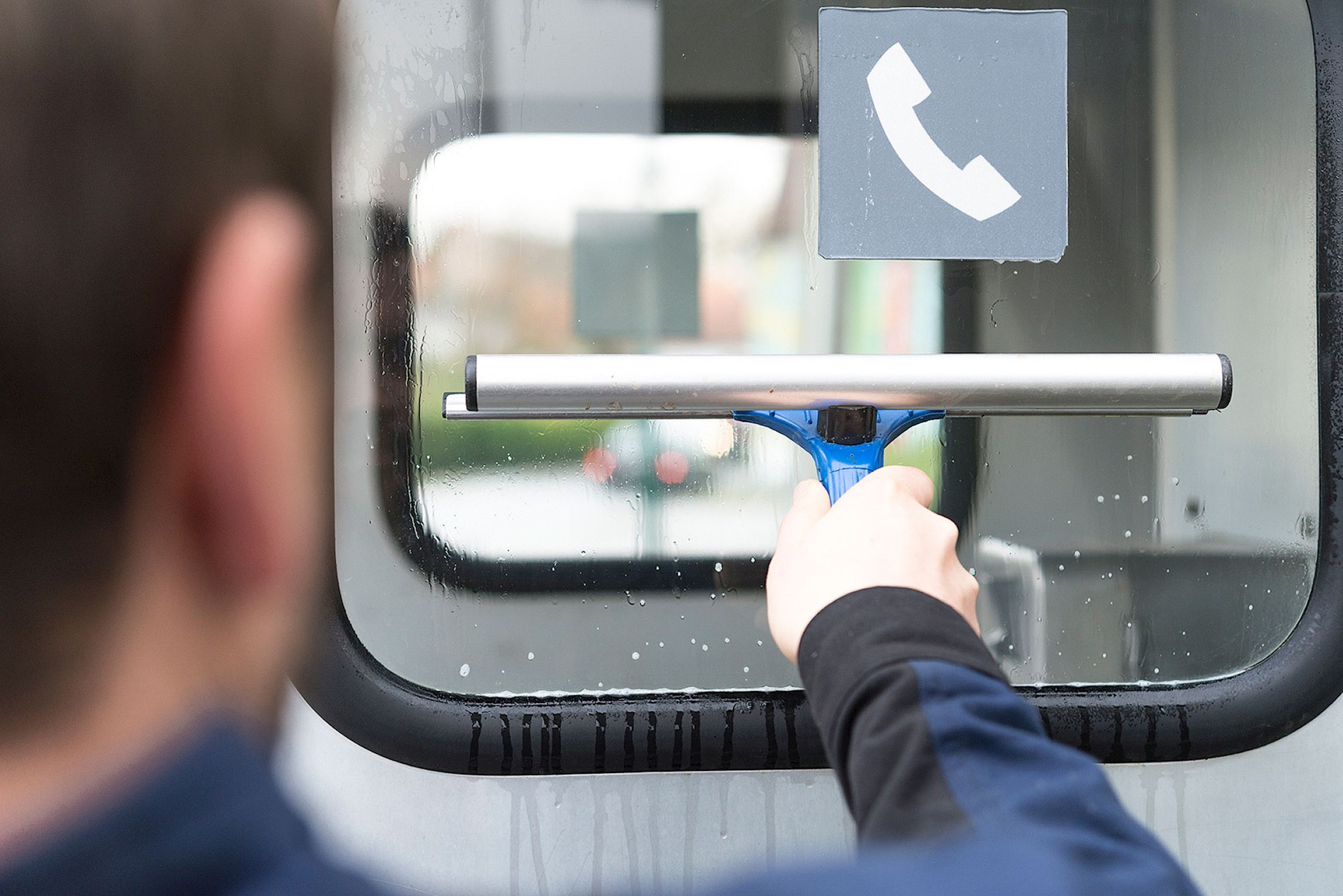 A person is cleaning the window of a phone booth.